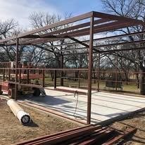 A metal structure is being built in a field with trees in the background.