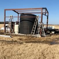 A large black tank is sitting under a metal structure in a field.