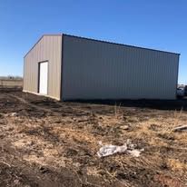 A metal building is sitting in the middle of a dirt field.