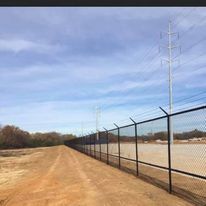 A chain link fence along a dirt road with power lines in the background.