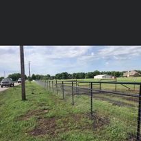 A fence surrounds a grassy field next to a road.