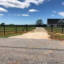 A driveway with a fence and a gate leading to a house.