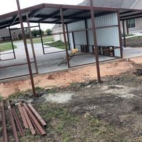 A metal structure is sitting in the middle of a dirt field next to a house.