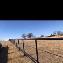 A fence surrounds a dry grass field with trees in the background.