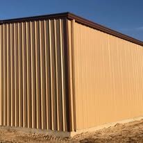 A large metal building with a brown roof is sitting in the middle of a dirt field.
