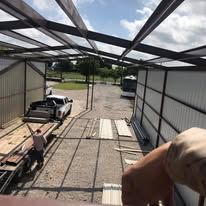A man is standing in front of a building with a truck in the back.