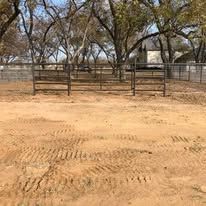 A dirt road with a fence and trees in the background.