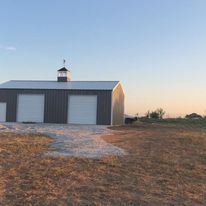 A large barn with a tower on top of it is sitting in the middle of a field.