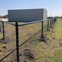 A fence is surrounding a grassy field with a building in the background.