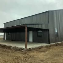 A large metal building with a covered porch is sitting on top of a dirt field.