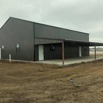 A large metal building with a covered porch is sitting in the middle of a dirt field.