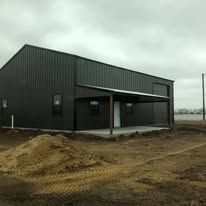 A black metal building with a porch is sitting in the middle of a dirt field.