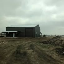 A large black building is sitting in the middle of a dirt field.