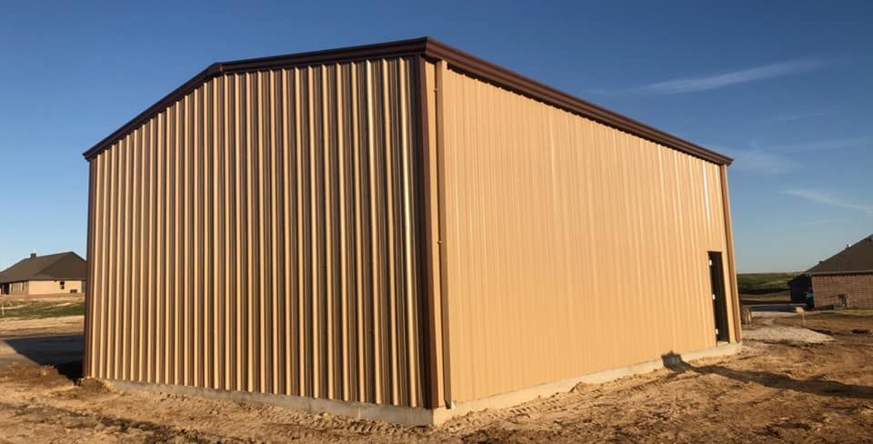 A large metal building is sitting in the middle of a dirt field.