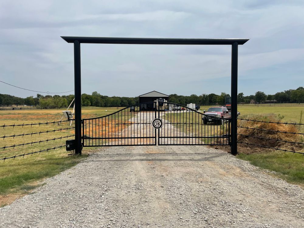 A metal gate is sitting on the side of a gravel road.