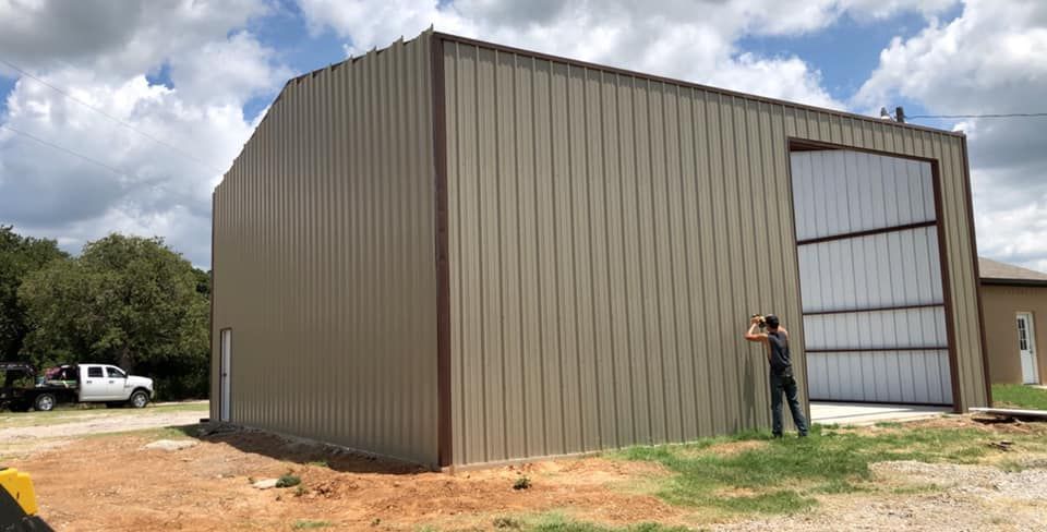 A man is standing in front of a large metal building.