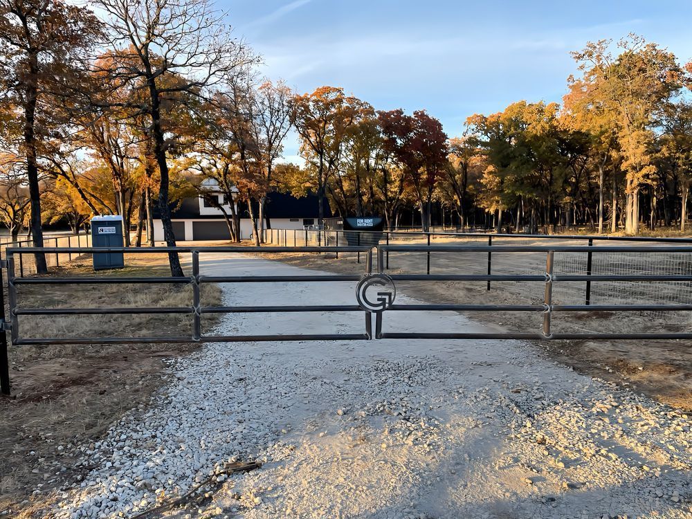 A metal gate leading to a dirt road with trees in the background.