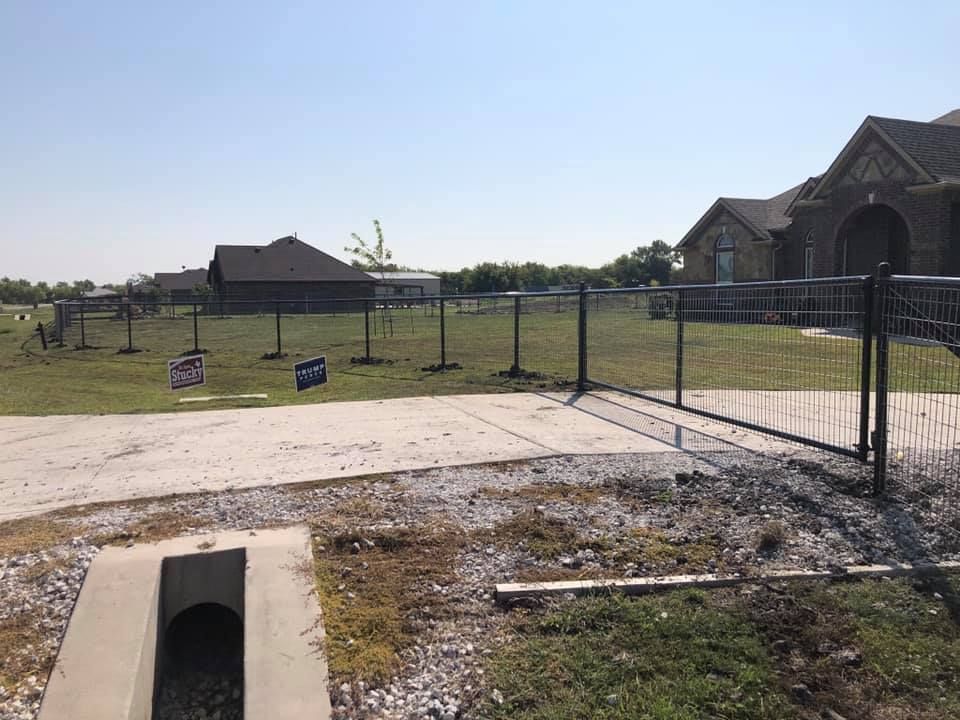 A fence is surrounding a grassy field in front of a house.