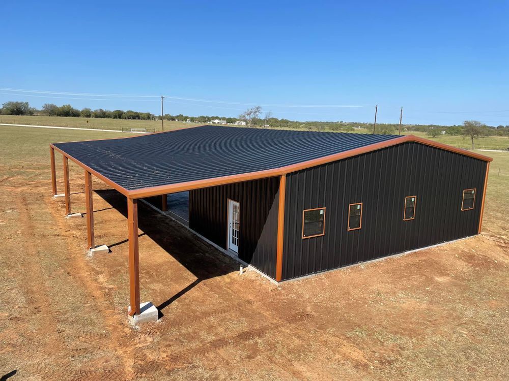 A large black metal building with a wooden frame is sitting in the middle of a field.