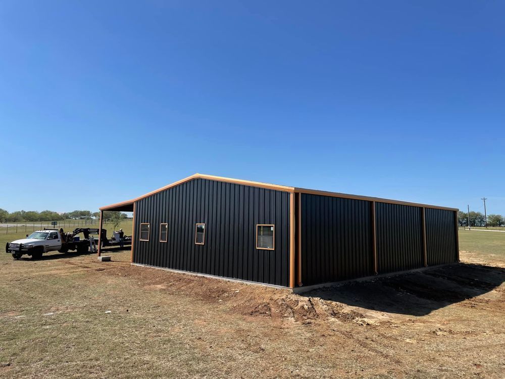 A large black metal building is being built in a field.