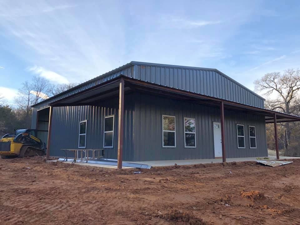 A large metal building with a porch is being built in a dirt field.