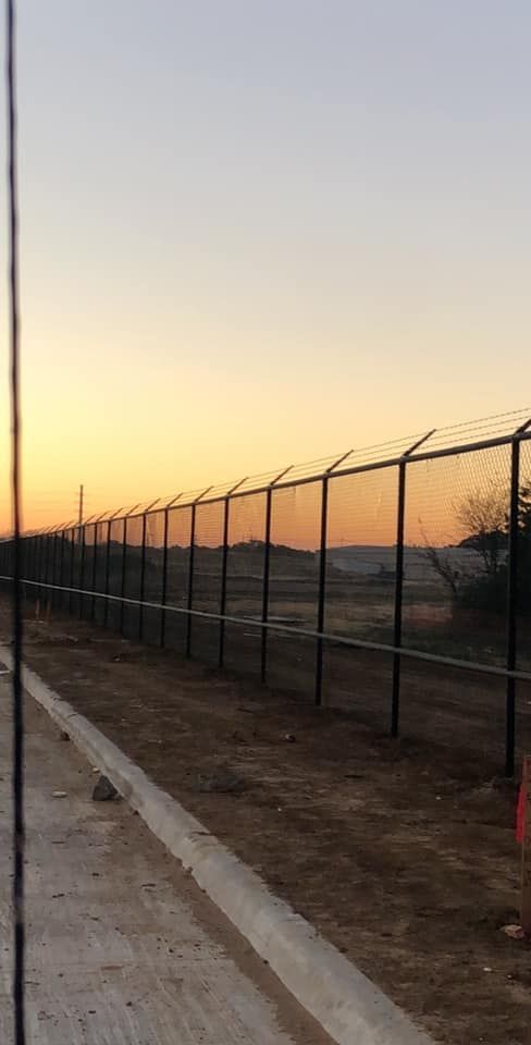 A chain link fence surrounds a dirt field at sunset.