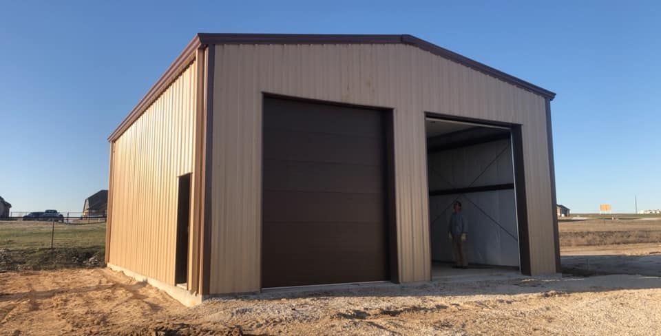 A metal garage with a brown door is sitting in the middle of a dirt field.