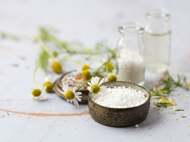 Una ciotola di globuli omeopatici accanto a una bottiglia di globuli omeopatici e margherite.