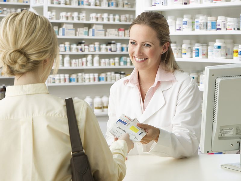 Una farmacista sta consegnando una scatola di pillole a una donna in farmacia.