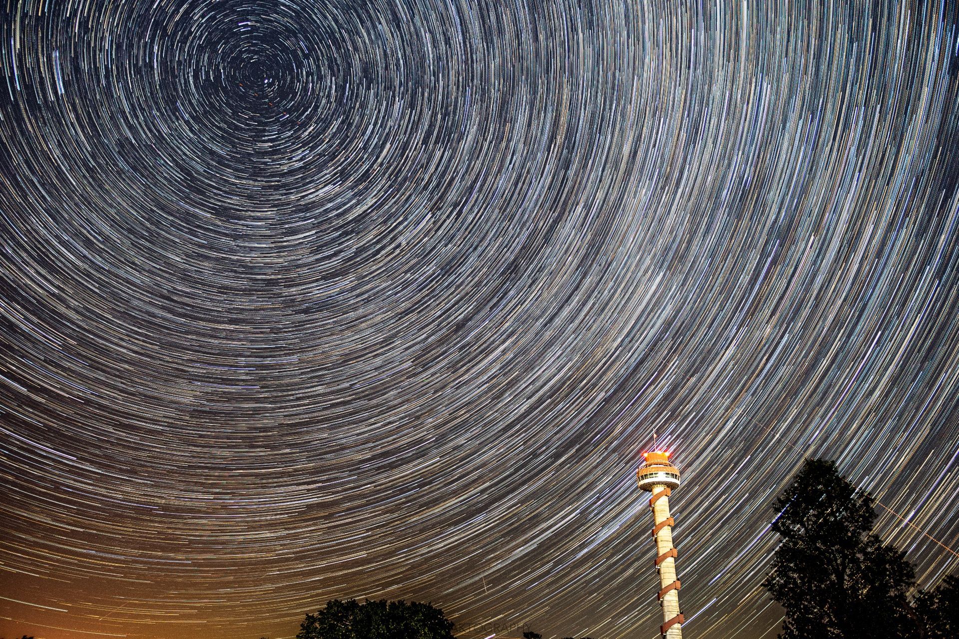 A lighthouse stands in the middle of a starry night sky.