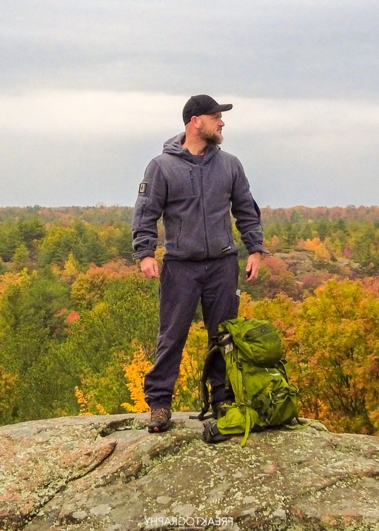 A man is standing on top of a rock with a backpack.