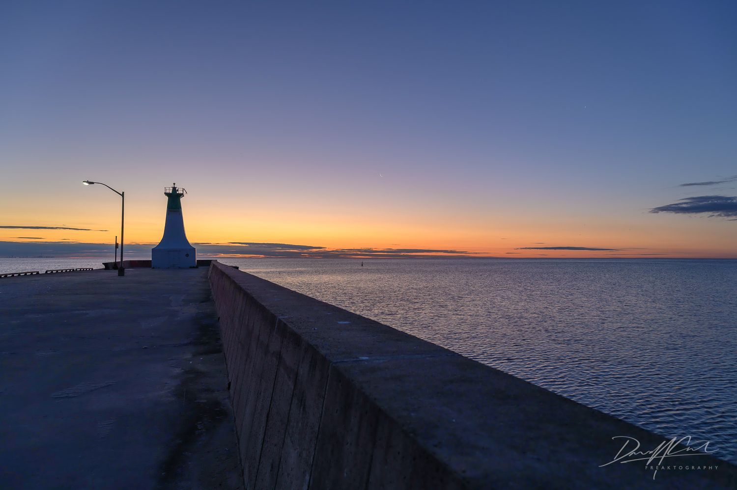 A lighthouse on a pier overlooking the ocean at sunset.