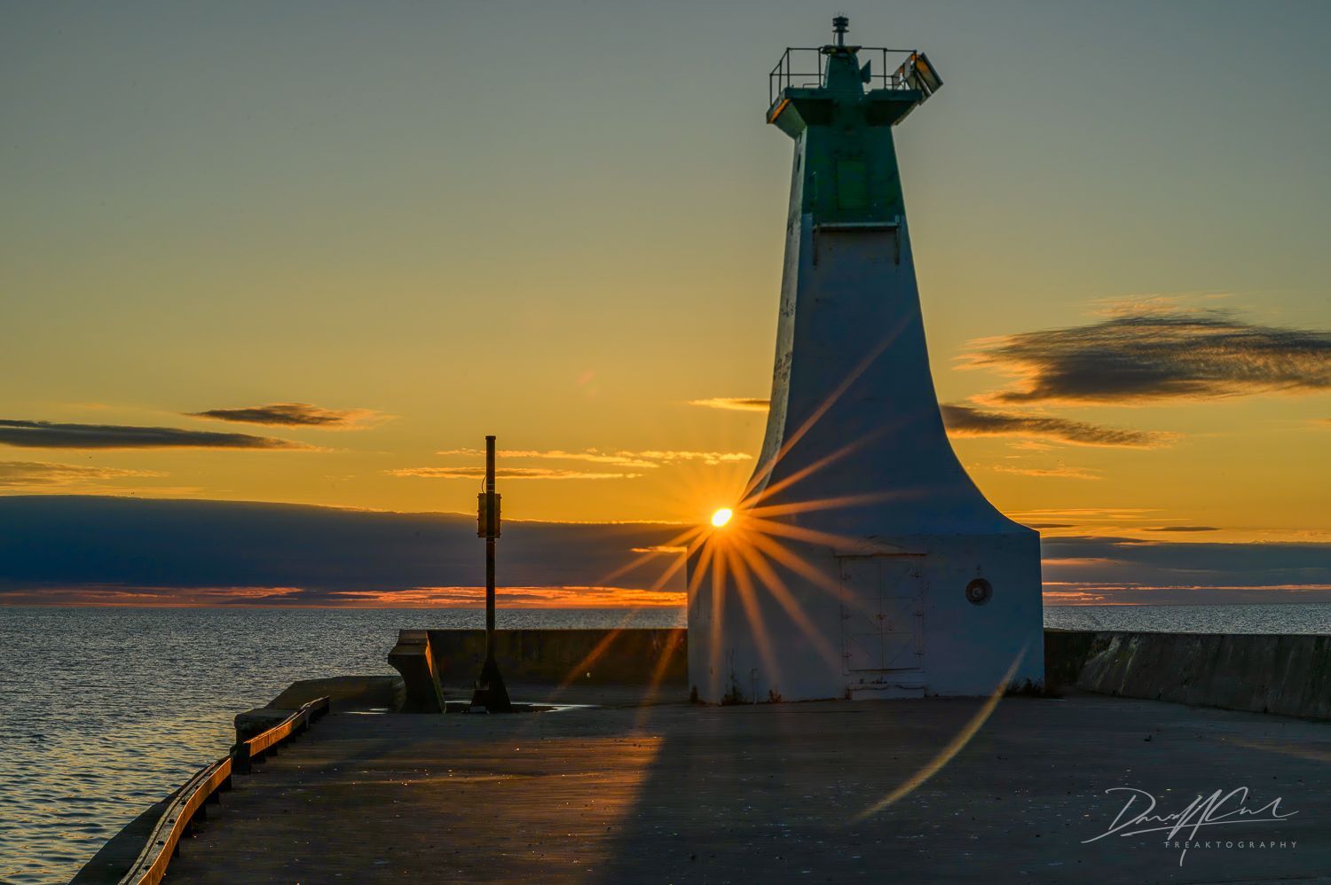 The sun is setting behind a lighthouse on a pier.
