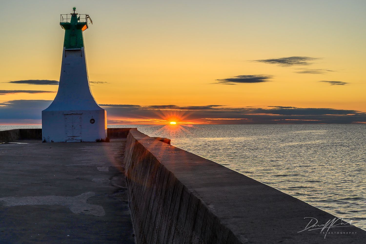 A lighthouse on a pier overlooking the ocean at sunset.