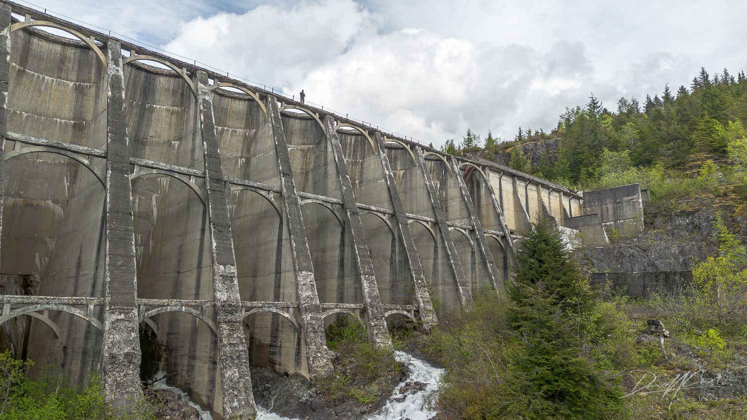 A large stone wall surrounded by trees and a river.
