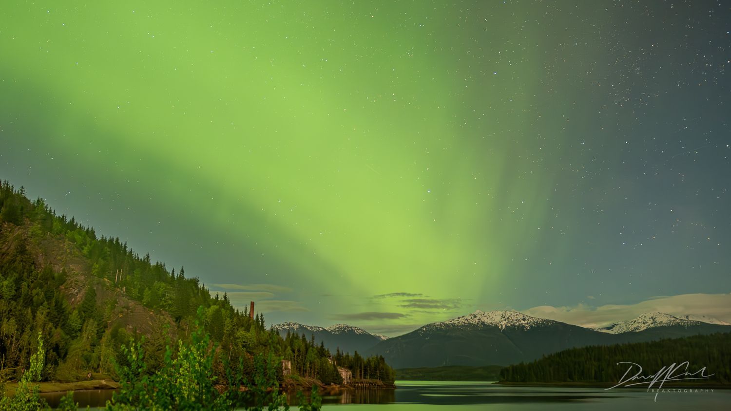 The aurora borealis is shining over a lake with mountains in the background.