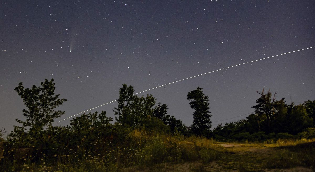 A satellite is flying through the night sky over a field of trees.