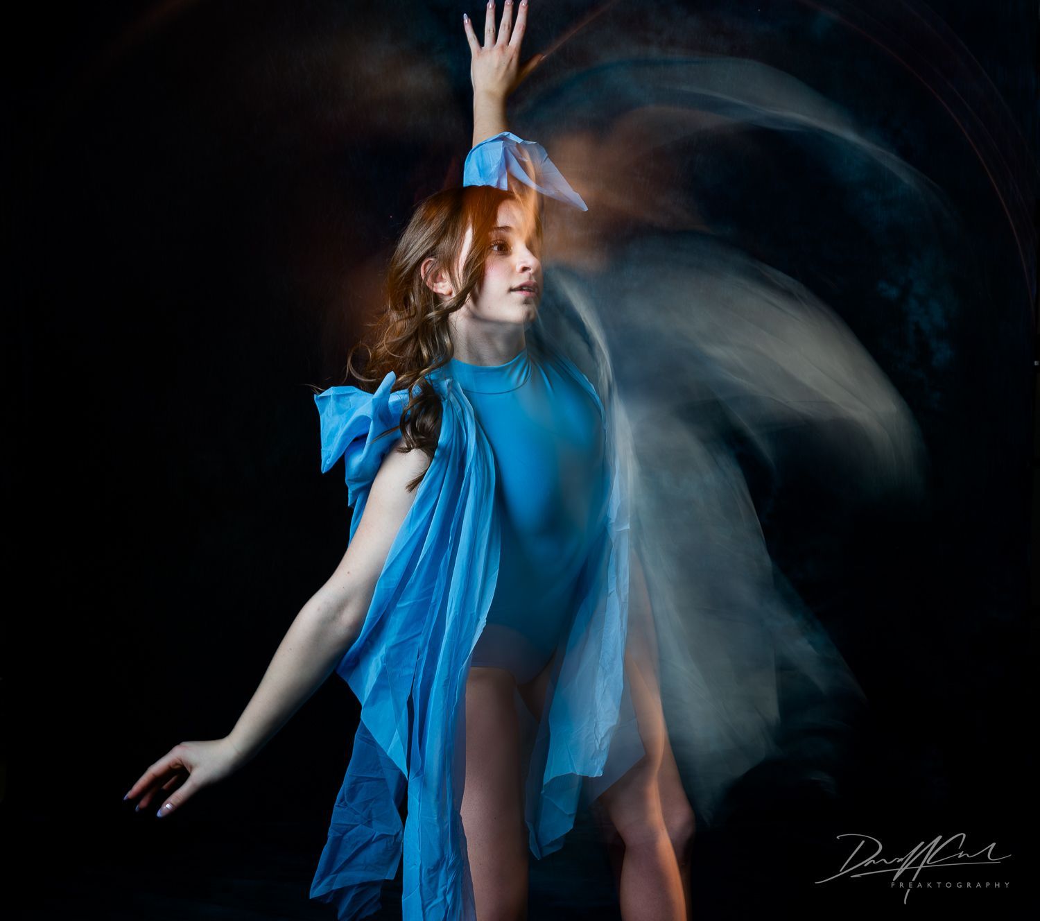 Ballerina in blue caught mid-dance with flowing fabric and motion blur against a dark studio background