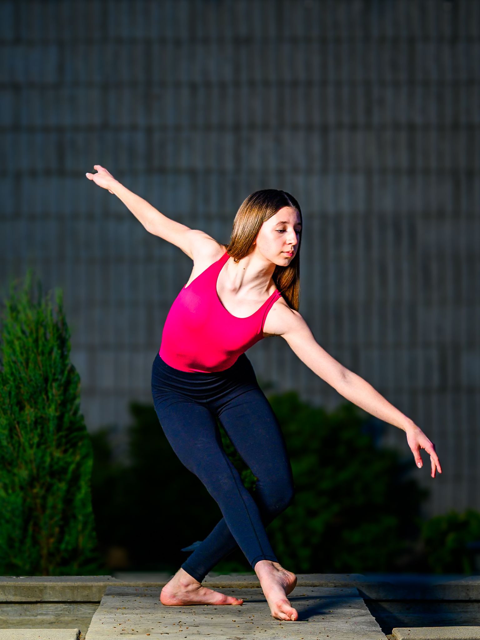 Ballerina Peyton in a red top and black leggings dancing barefoot outdoors, arms extended in a graceful pose