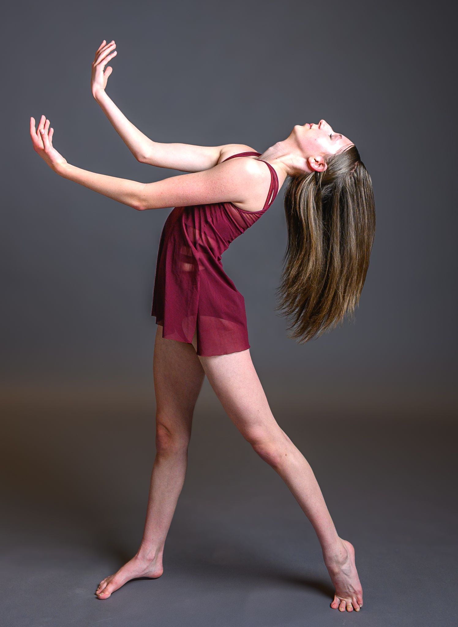 Ballerina Peyton in a maroon dress leaning back with arms extended in a dramatic dance pose, studio background