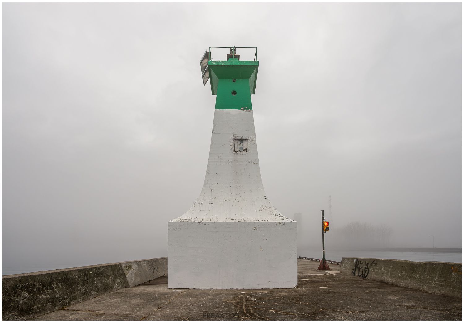 A green and white lighthouse on a foggy day