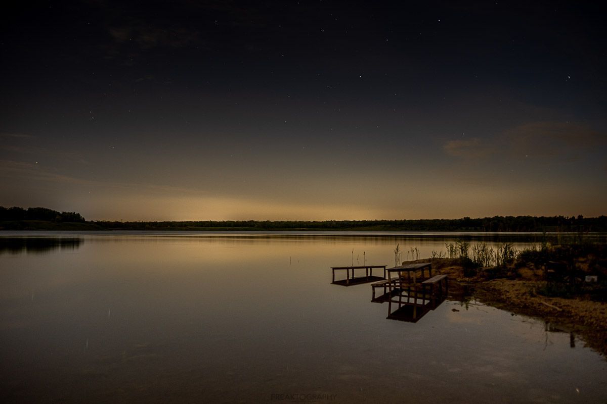 There is a dock in the middle of the lake at night.