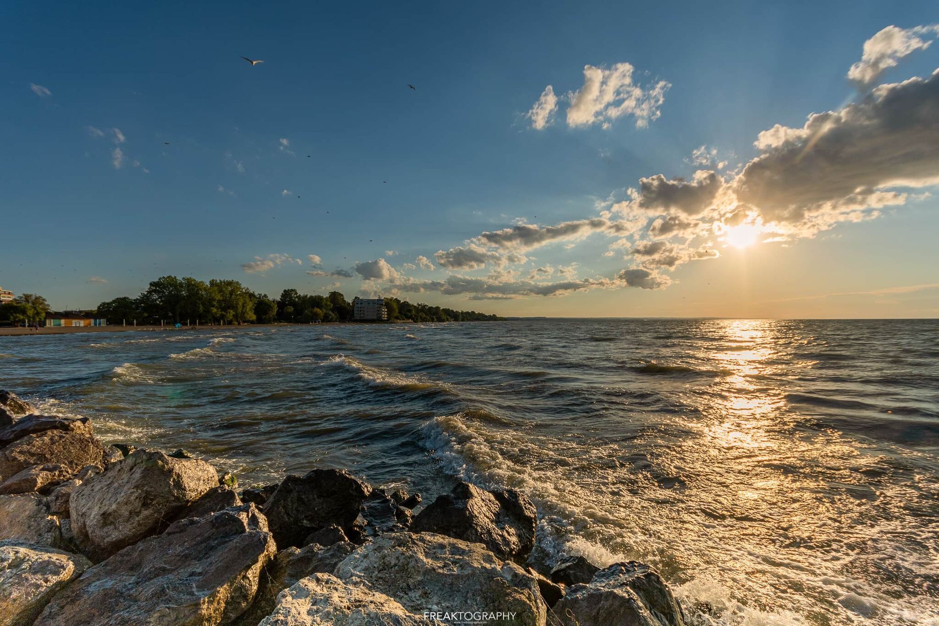A sunset over a large body of water with rocks in the foreground.