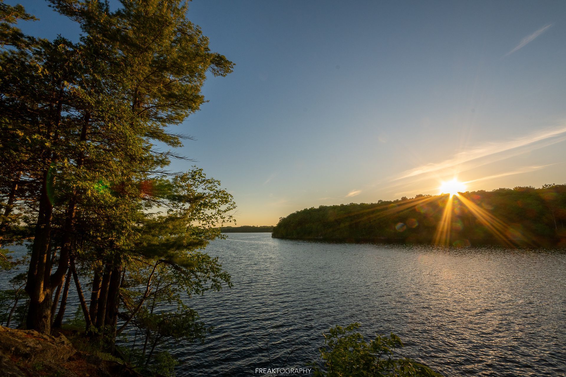 The sun is setting over a lake with trees in the foreground