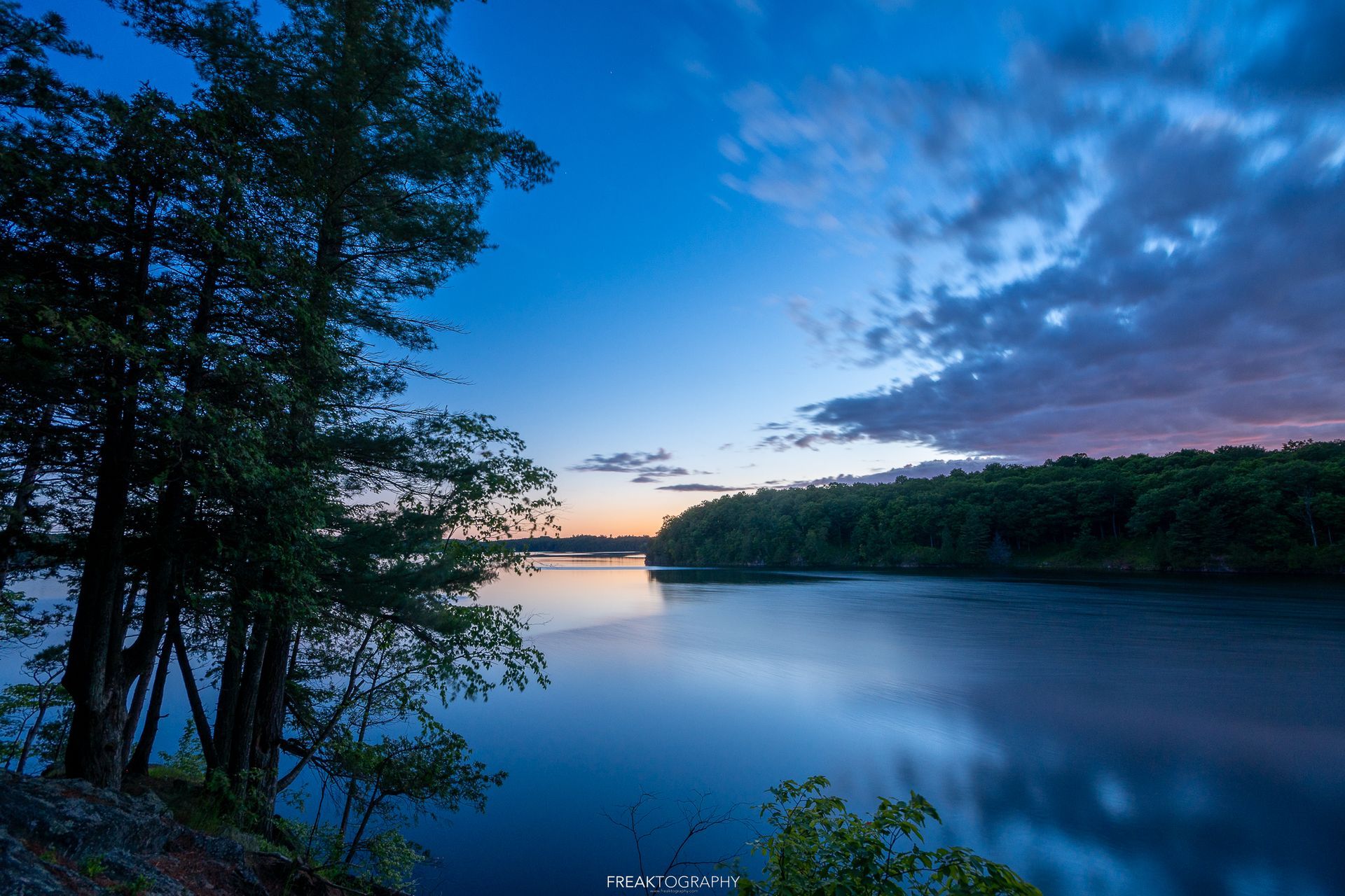 A lake with trees in the foreground and a sunset in the background