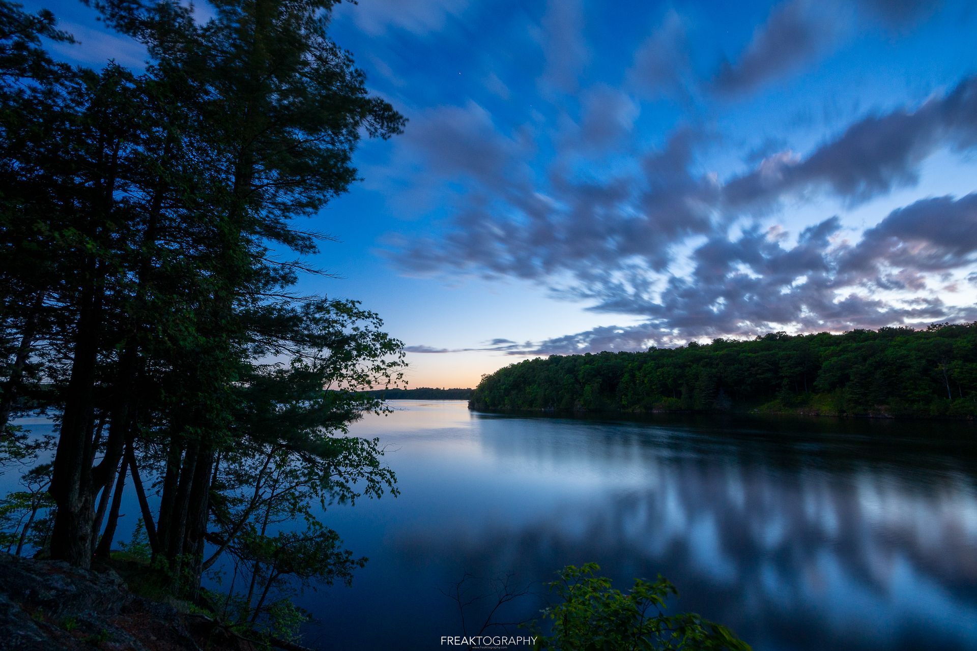 A lake with trees on the shore and a blue sky with clouds