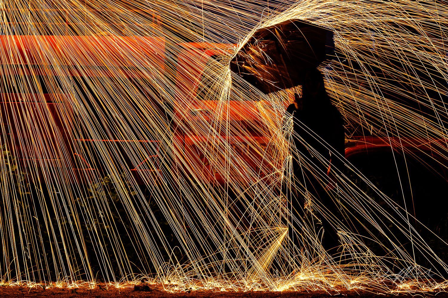 Girl holding umbrella under steel wool sparks in front of abandoned red fire truck