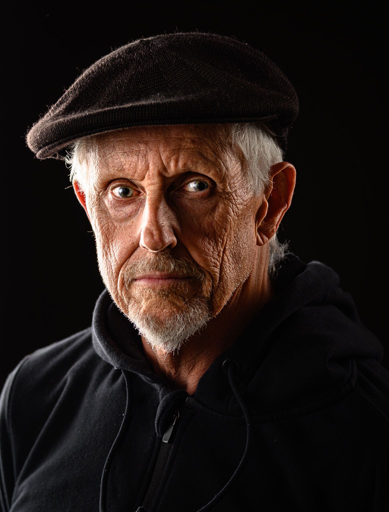 Portrait of an elderly man in black hoodie and cap with dramatic lighting