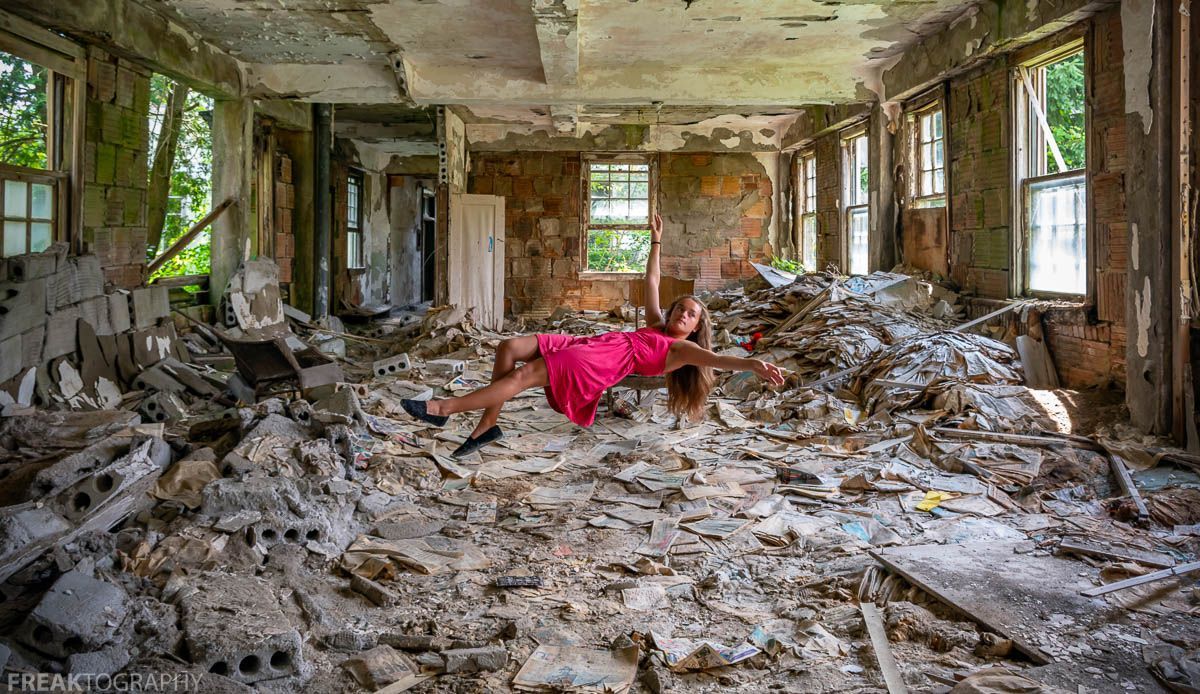 Woman levitating in pink dress inside abandoned building with rubble and newspapers