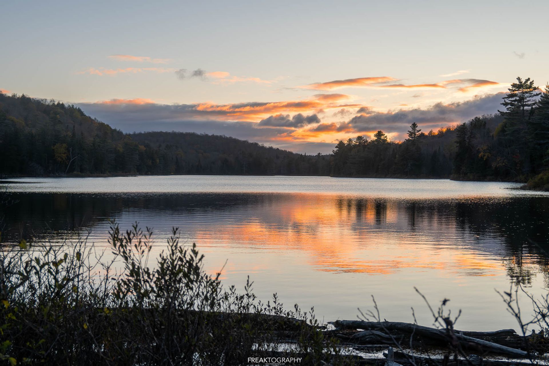 A lake with a sunset in the background and trees in the foreground
